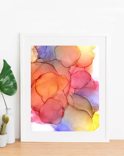 Sundrenched Glow painting displayed in a white frame propped up against a white wall, on a wood table with a small vase and planter on the left.