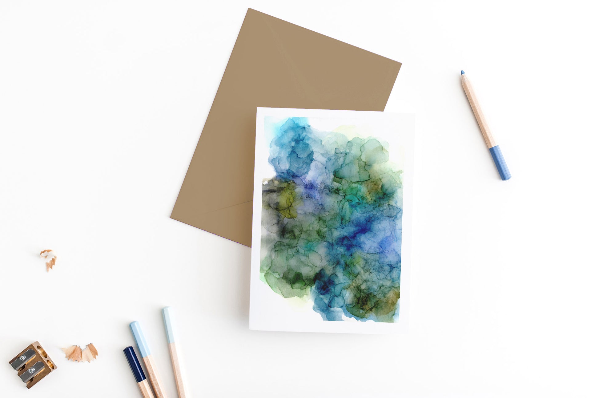 Greeting card, seen from above, with a colored, square flap envelope, pencils, pencil sharpener and shavings on a white background.