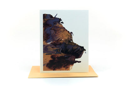 Greeting card showing an abstract painting in golds, dusty blues, and browns created from squishing acrylic paint between pieces of cardboard. It sits on a gold envelope.