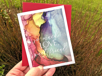 Hand holding a greeting card and kraft envelope in front of grasses outdoors.