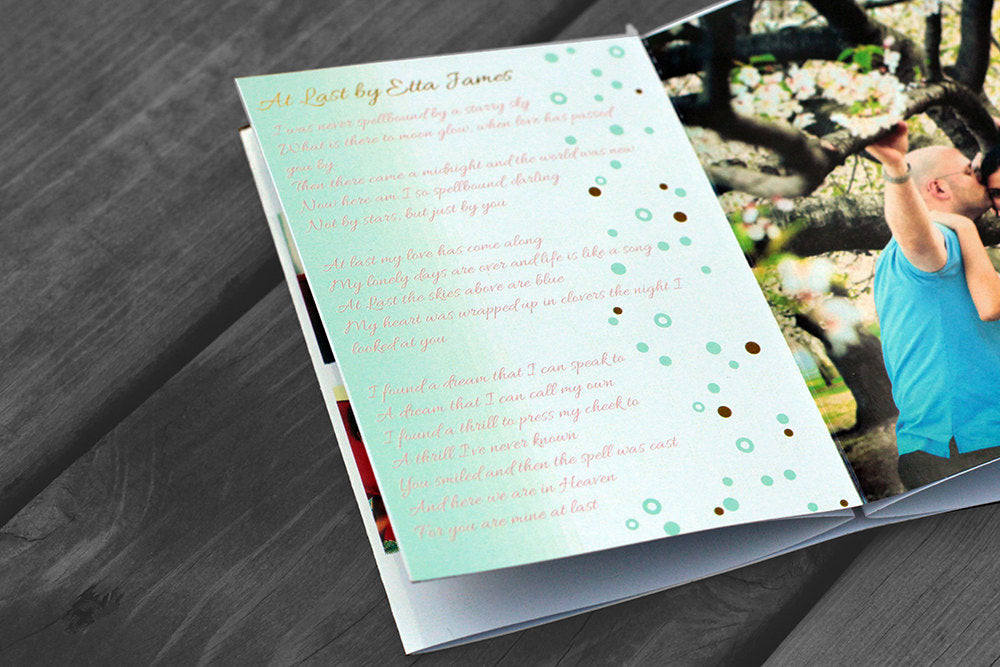 Centerpiece laying flat on wooden boards showing the couple kissing underneath the branches of a tree and a page of favorite song lyrics.